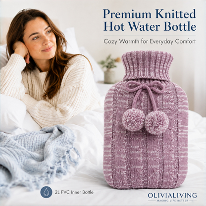 Pink Red OliviaLiving 2L hot water bottle with pom-pom knit cover beside a woman seated on a bed